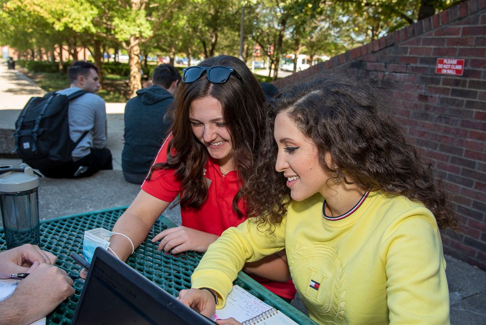 Two female students sitting at a picnic table outside of Muntz Hall